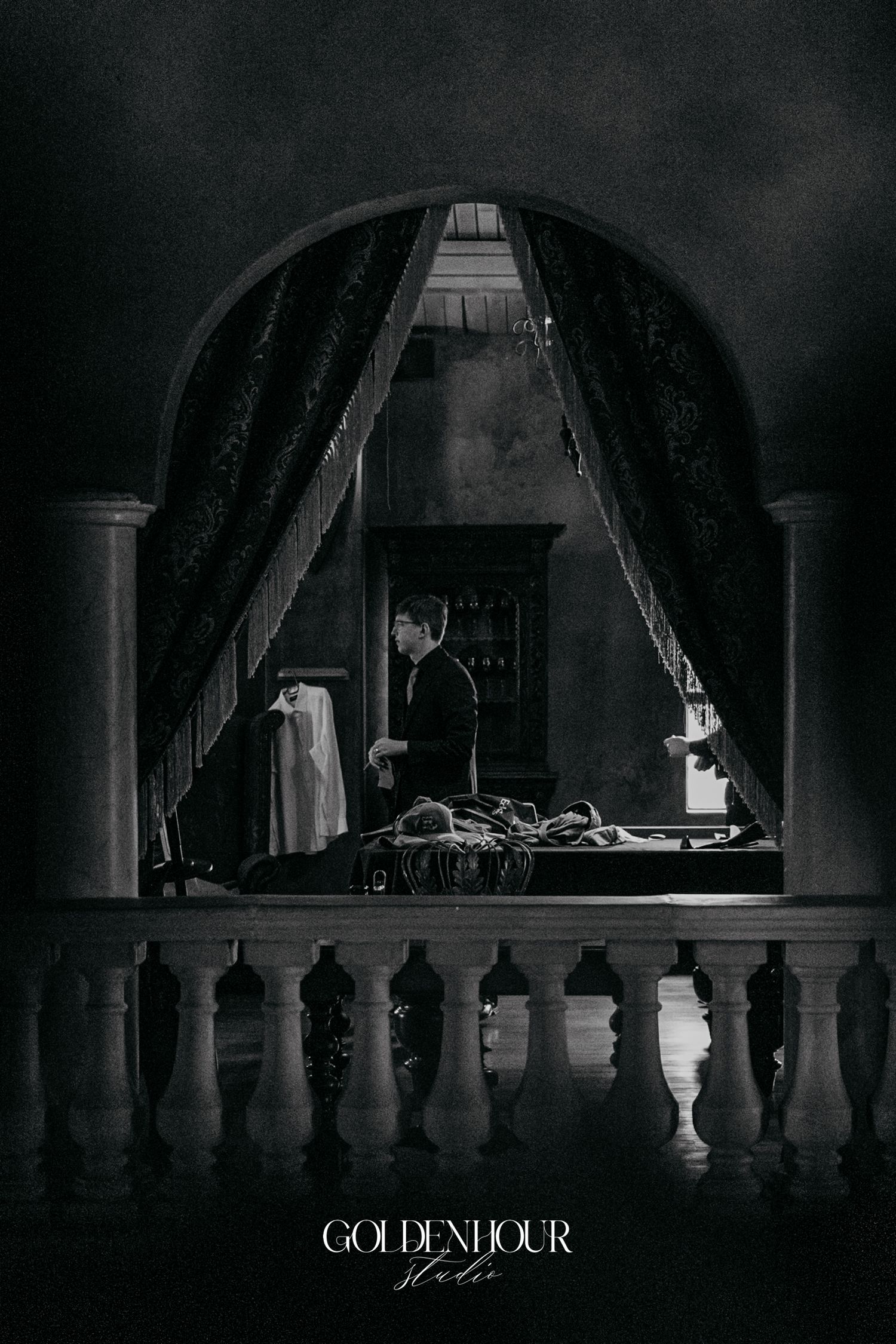 Dramatic black and white groom preparation photo framed by elegant arch and balustrade.