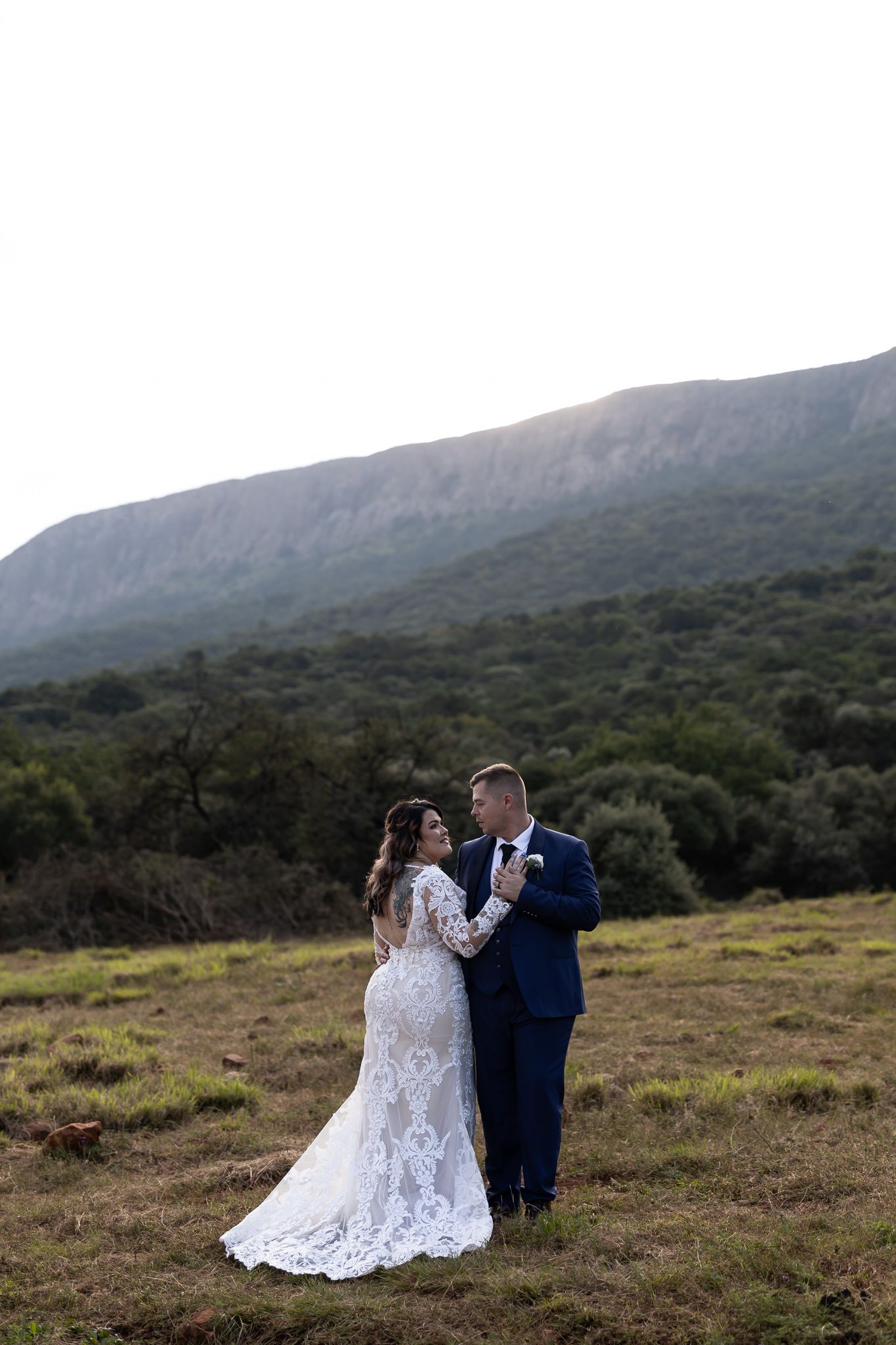 Newlyweds share an intimate moment in front of mountains during their outdoor wedding photoshoot.
