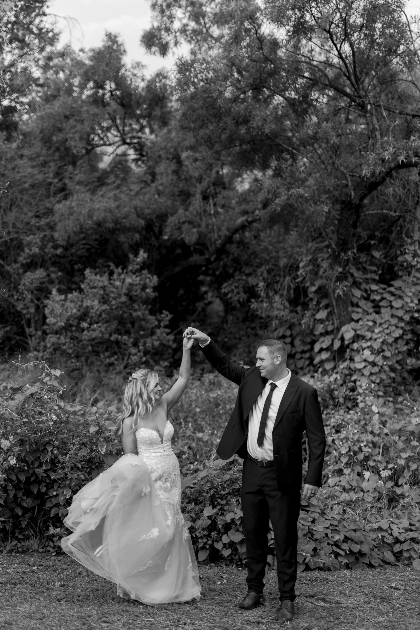 A black and white photo of a dancing couple in wedding attire outdoors.