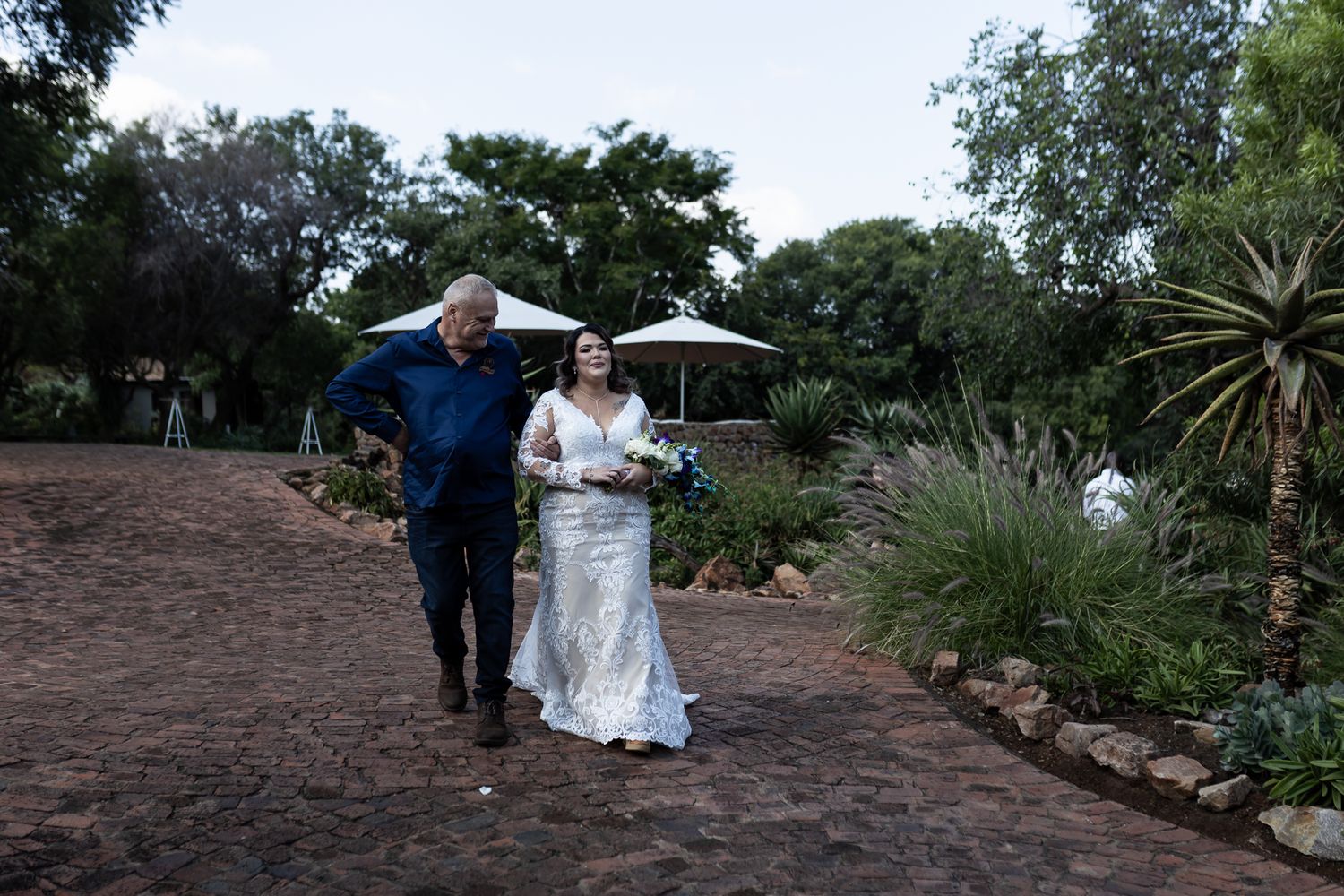 Couple walking along garden path at dusk during wedding celebration.