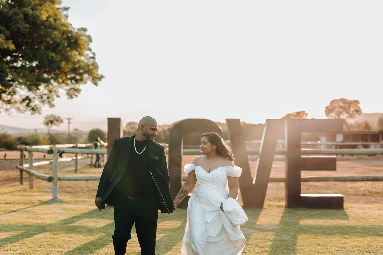 Couple walks hand in hand near large LOVE letters during golden hour at their outdoor wedding.