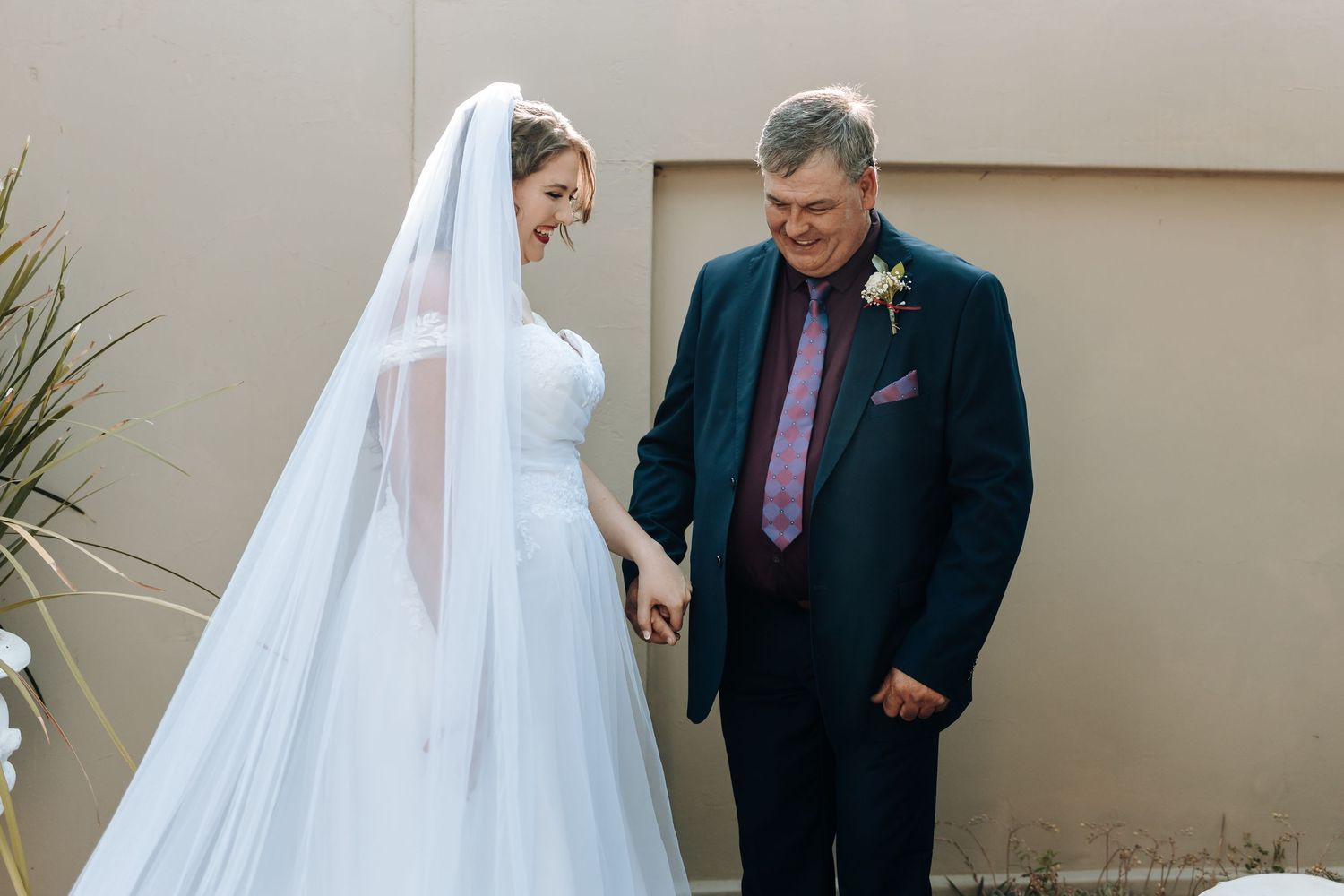 A touching wedding day moment captured outside against a neutral wall.
