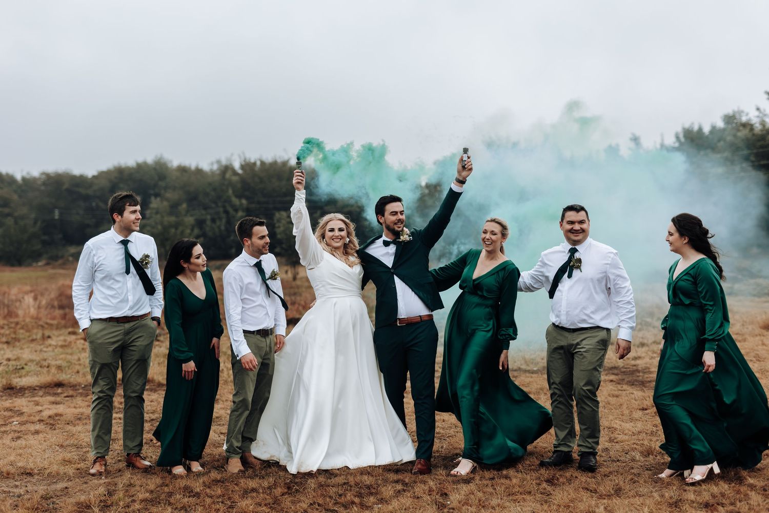 Wedding celebration with teal smoke bombs against rustic landscape backdrop.