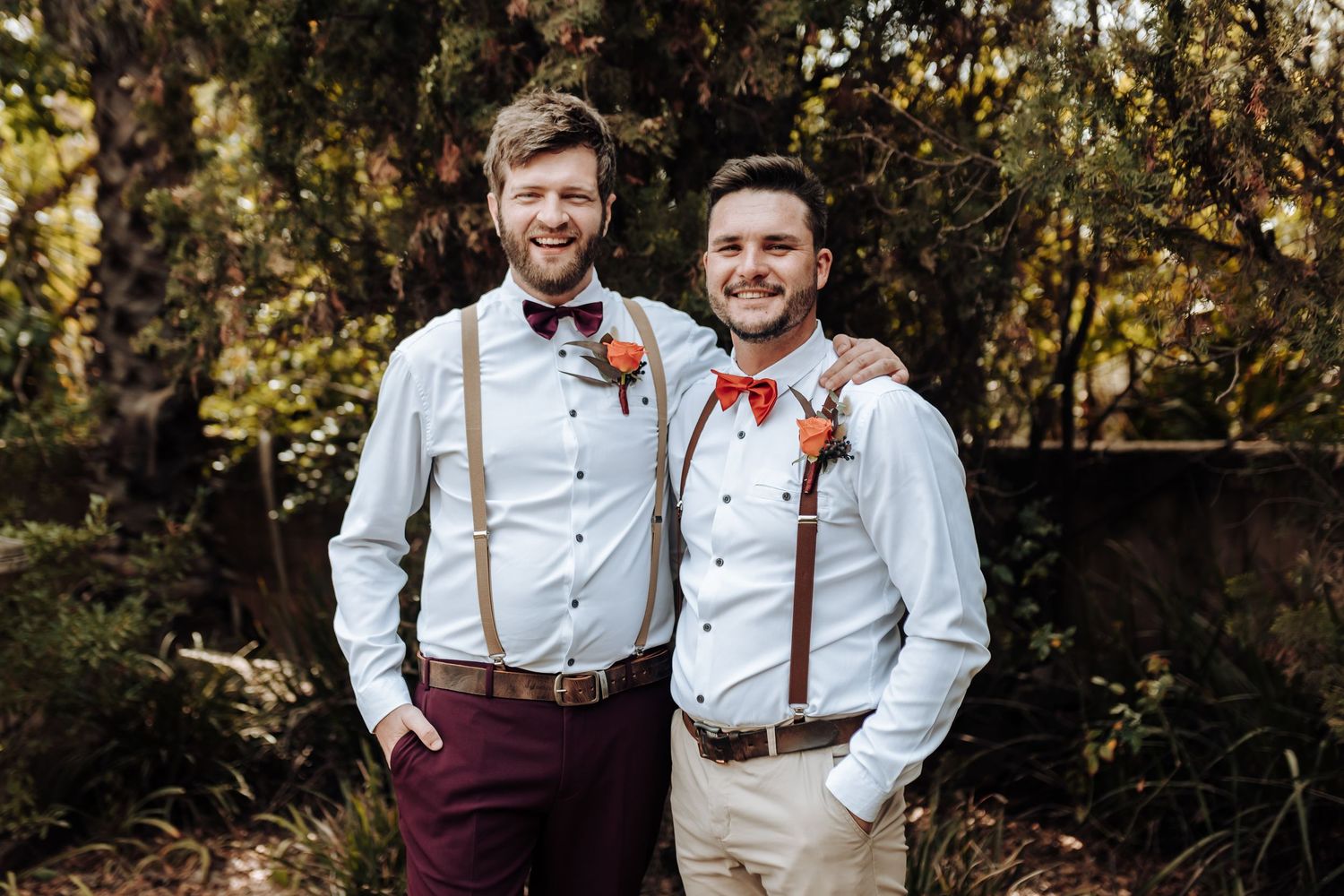 Wedding party members in matching suspenders and bow ties smile for a portrait outdoors.