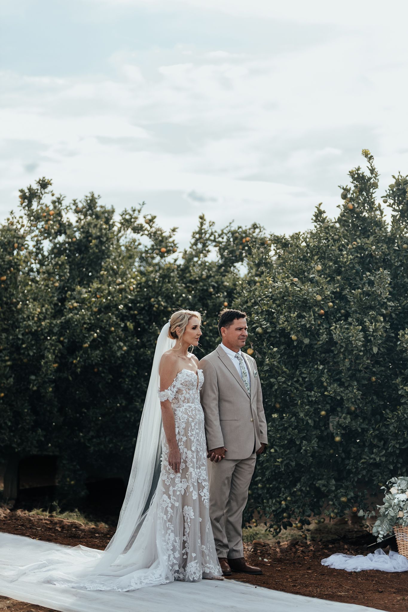 Couple standing together during outdoor wedding ceremony surrounded by citrus grove.