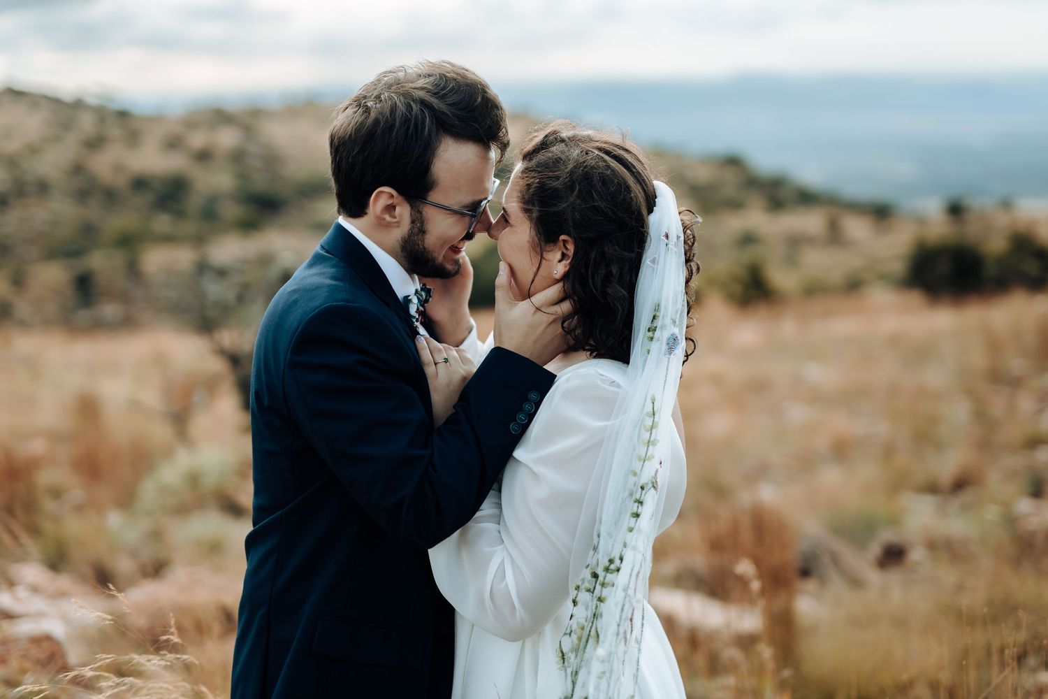 Romantic outdoor wedding portrait of couple kissing against desert landscape.