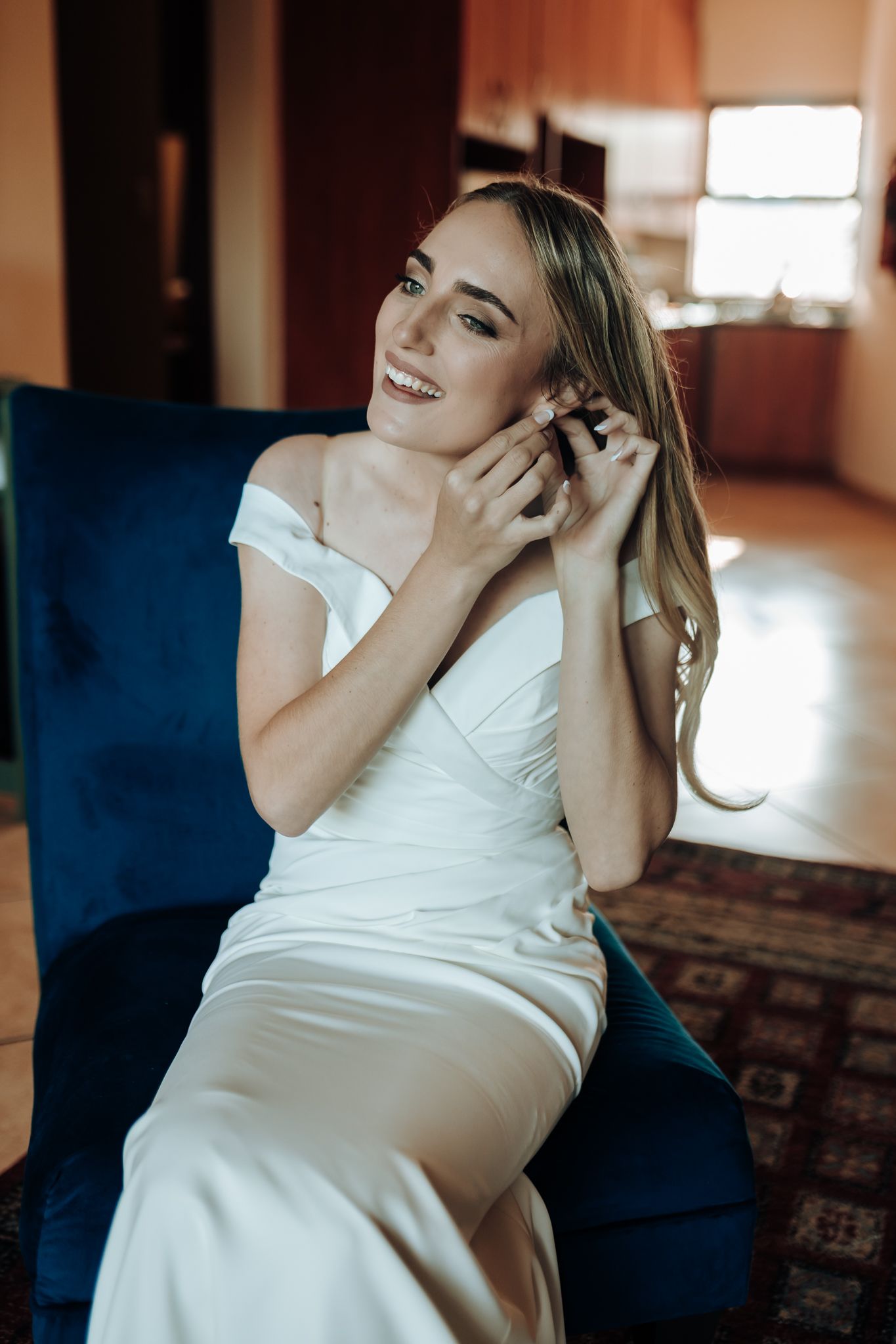 Candid moment of joy during wedding preparations in a sunlit room with blue chair.