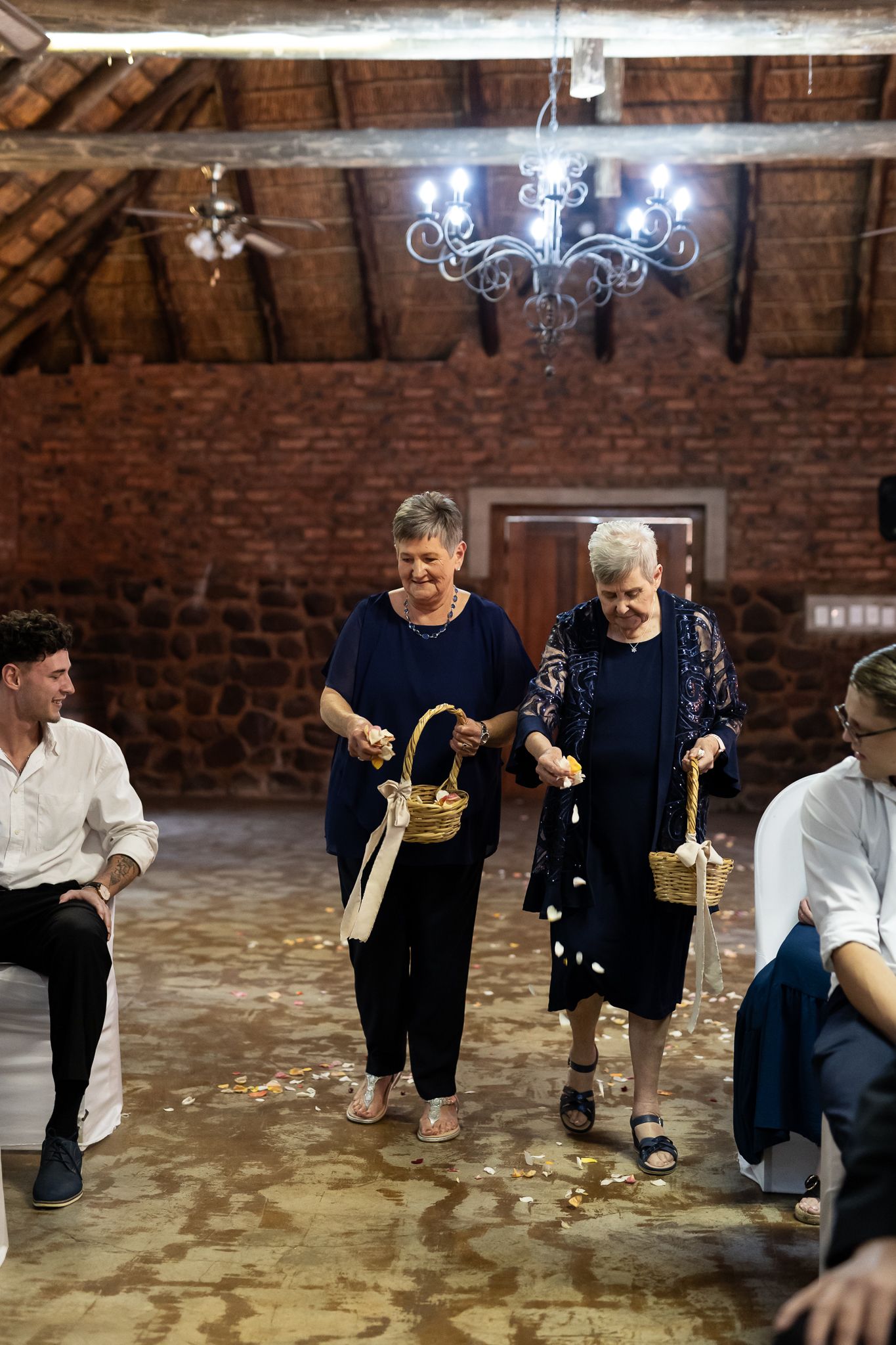 Wedding guests tossing flower petals in a rustic venue with exposed brick walls and chandelier.
