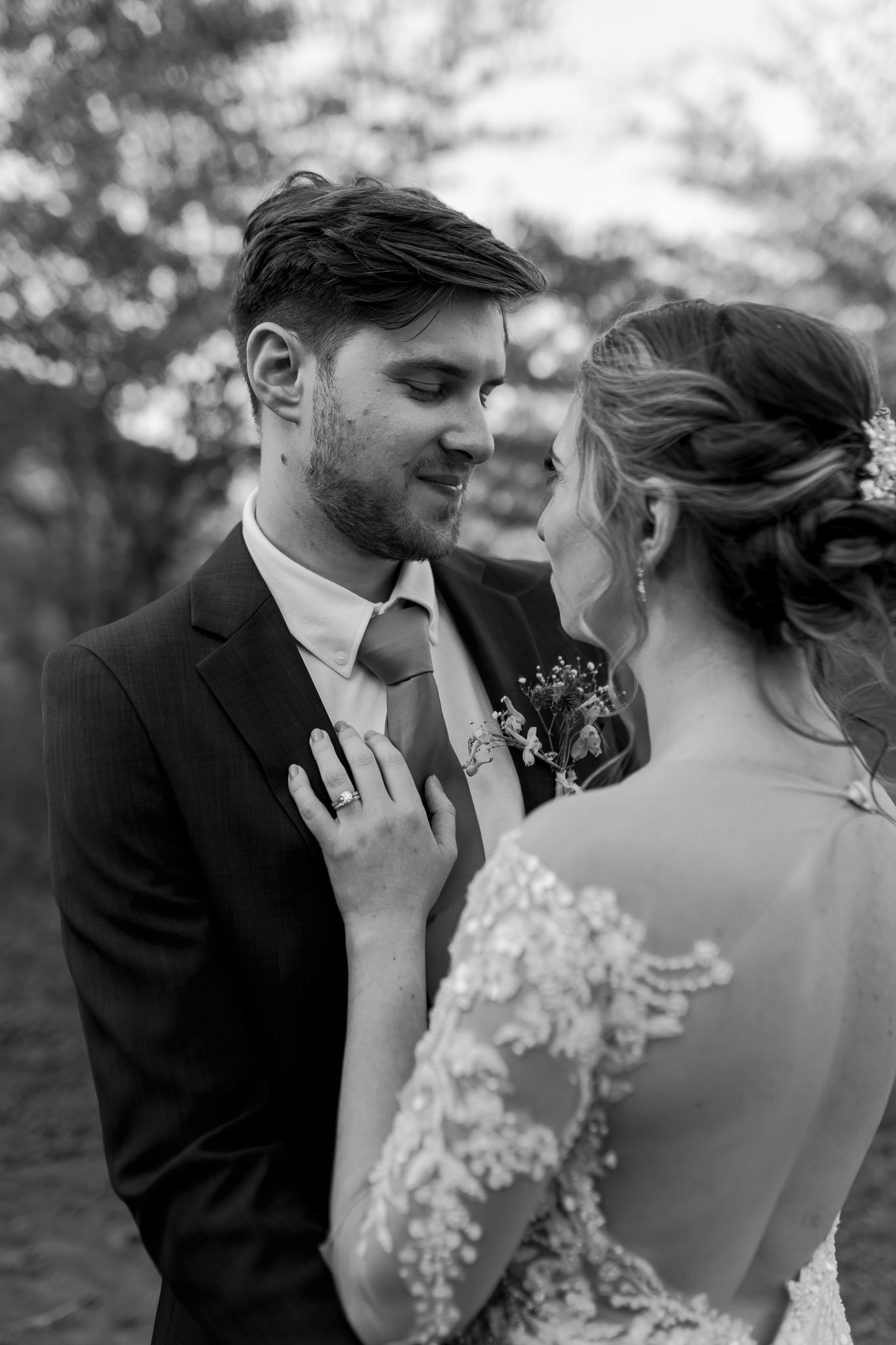 Intimate black and white portrait showing tender moment between newlyweds with detailed lace dress visible.