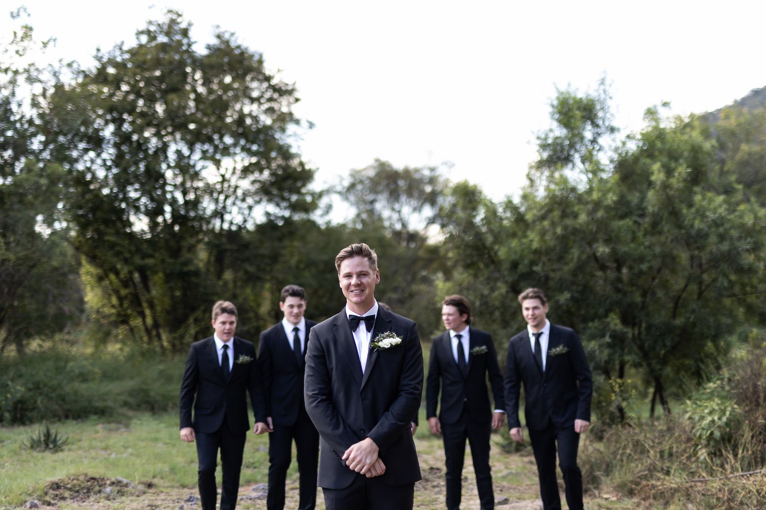 Formal wedding party portrait with groomsmen standing behind in an outdoor setting.