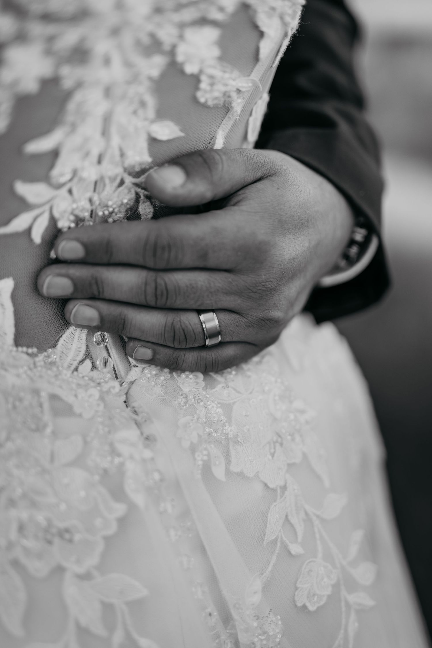 Black and white close-up shots of hands wearing wedding rings against delicate white lace details of a wedding dress.