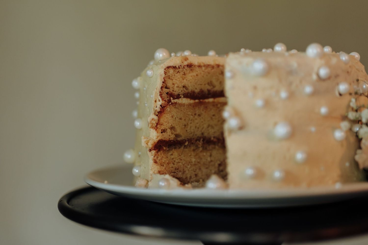 A slice of layered chocolate cake with caramel frosting and white pearl decorations on a black plate.
