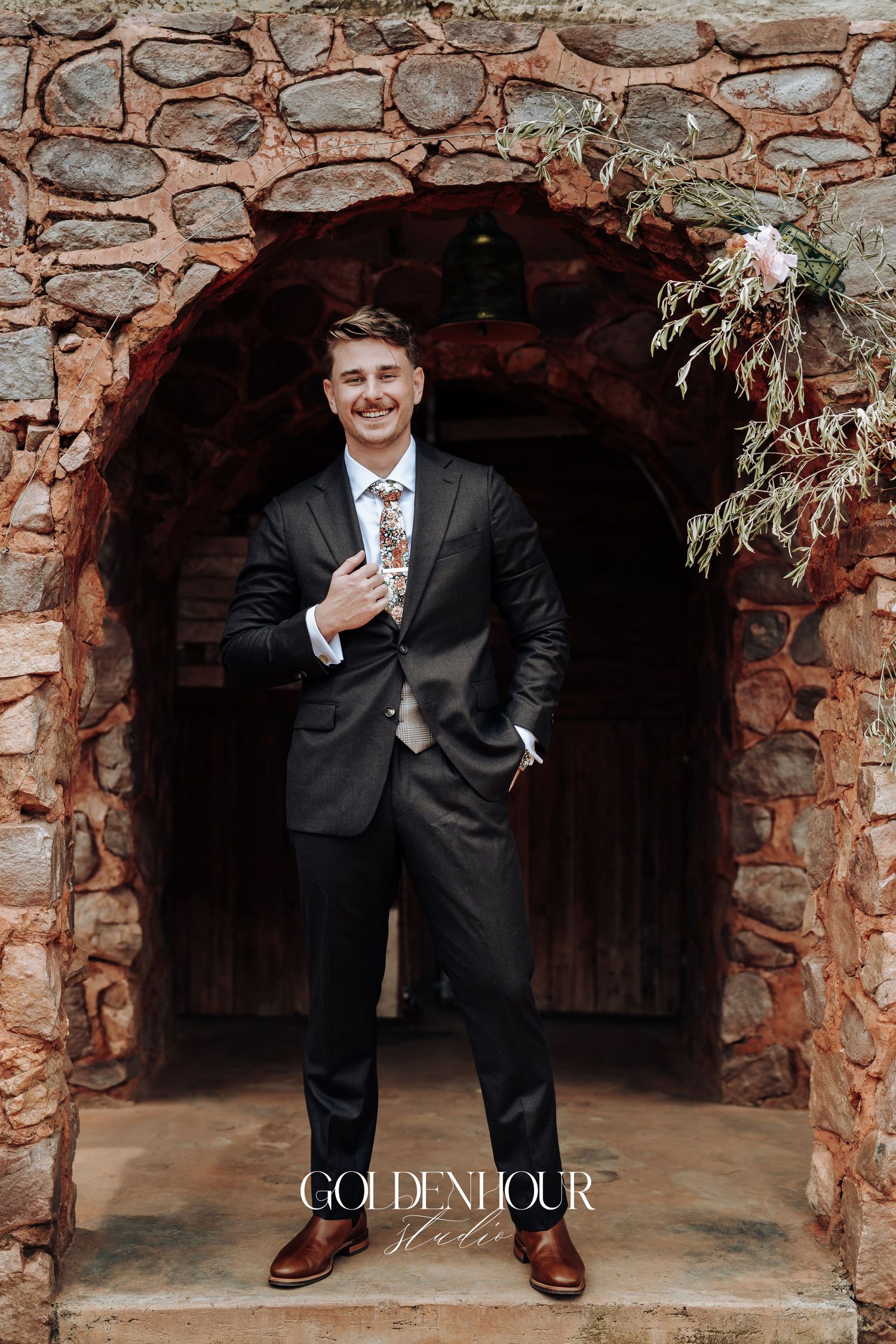 Two groomsmen pose playfully in front of a rustic stone wall structure.
