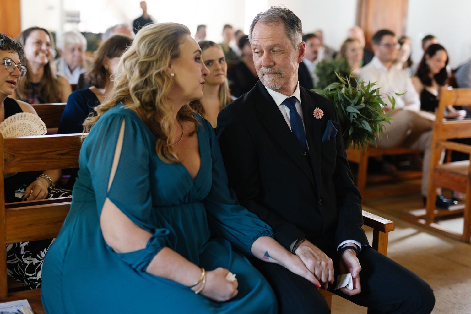 Couple sitting together in church pews during a wedding ceremony.