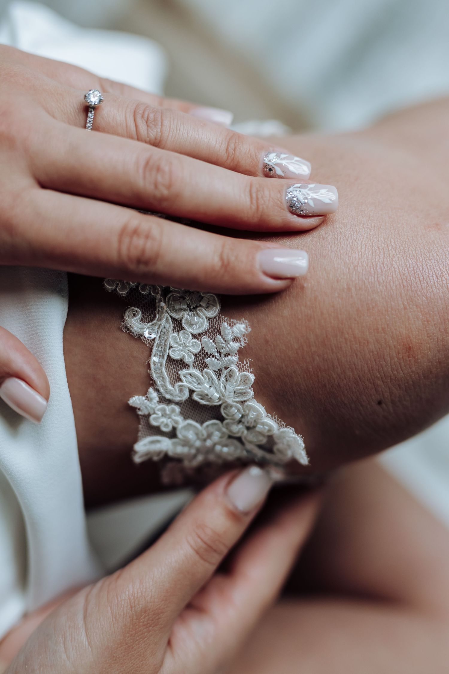 Close-up of elegant white lace detail on fabric with manicured nails and engagement ring visible.