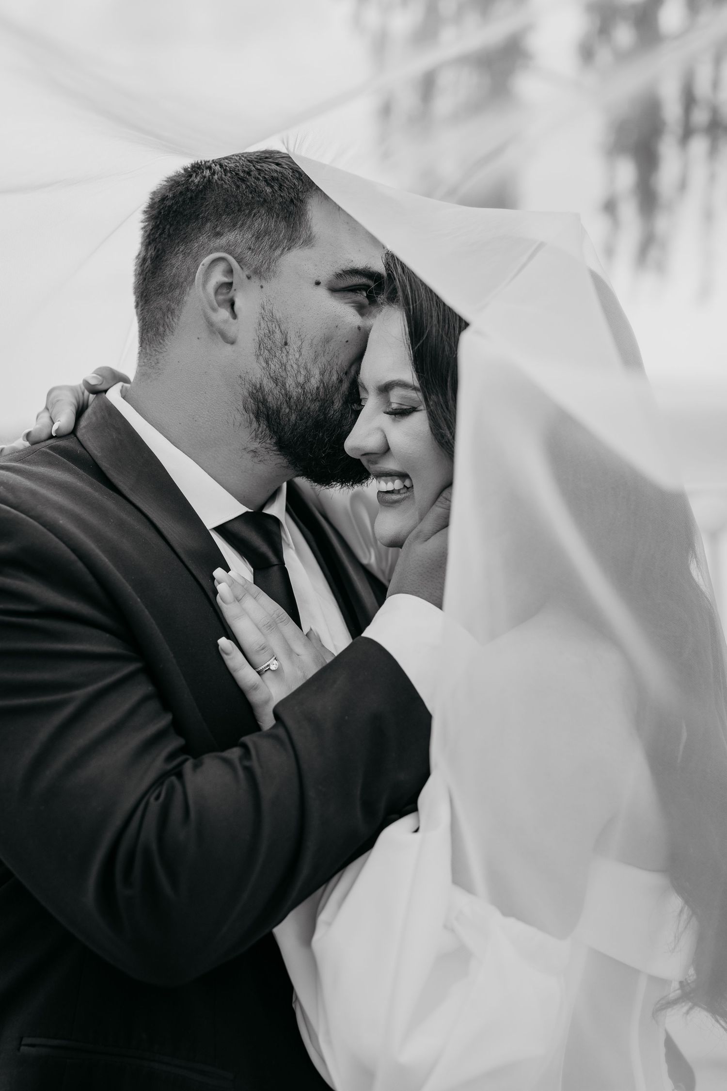 A tender black and white wedding photo showing an intimate moment under a flowing veil.