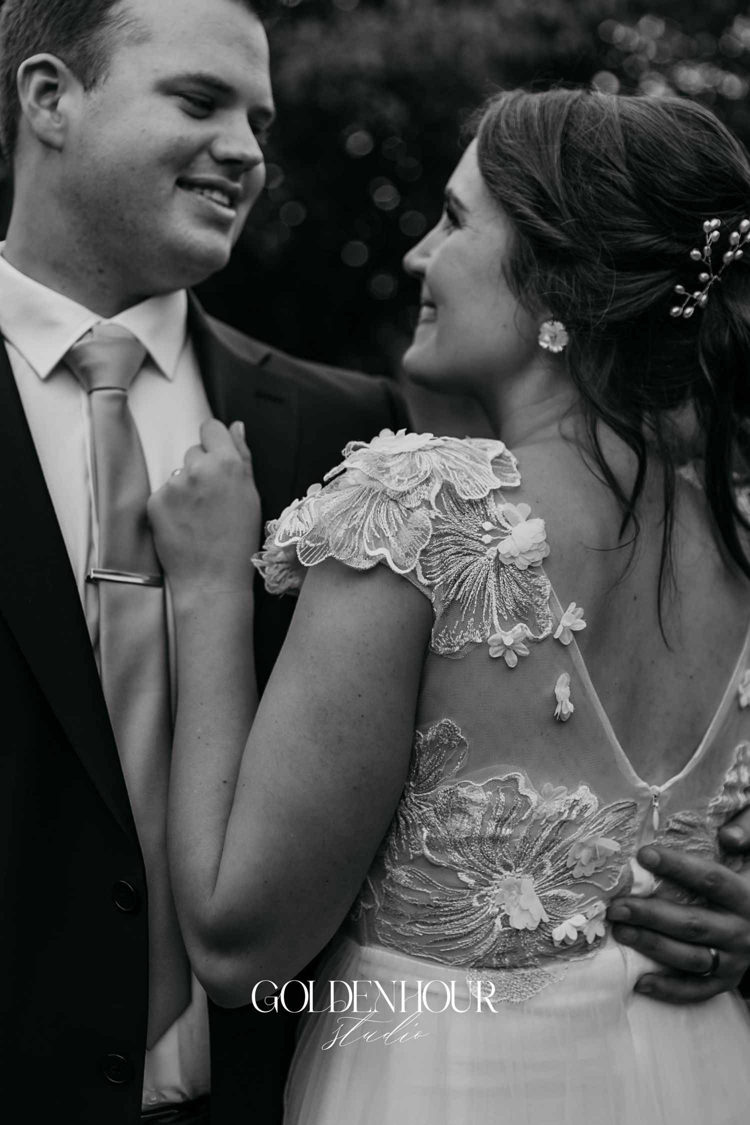 Black and white photo of a bride and groom sharing a tender moment, bride wearing a floral lace wedding dress.