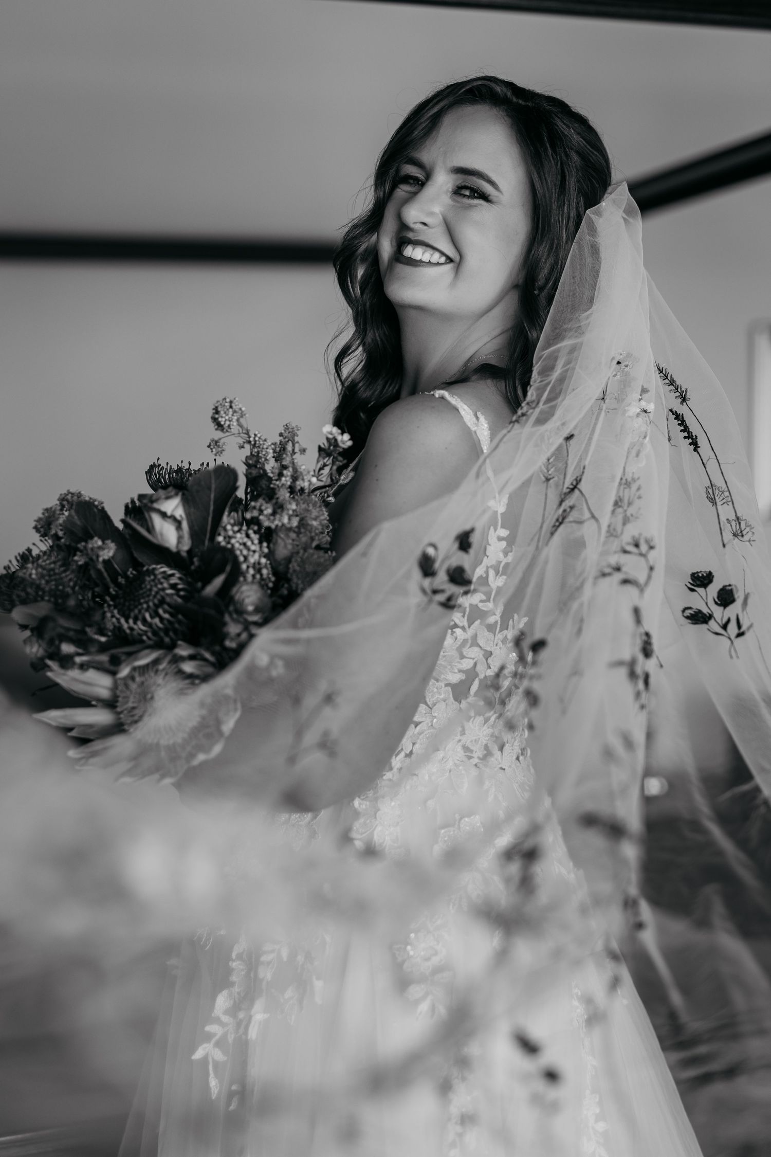 A bride in a delicate lace veil is shown in a black and white photo series expressing joyful emotions.