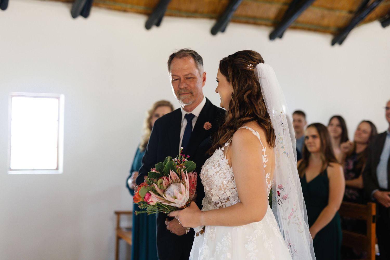A couple shares a romantic dance moment at their wedding reception in an elegant indoor venue with exposed wooden beams.