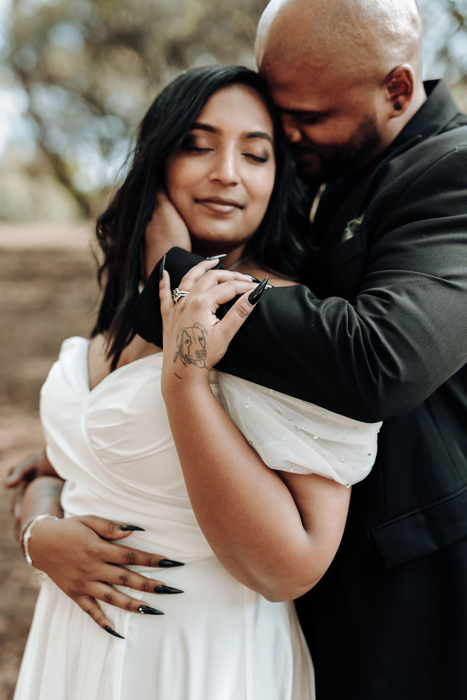 Intimate wedding couple embrace outdoors with bride in white dress and groom in black suit at sunset.