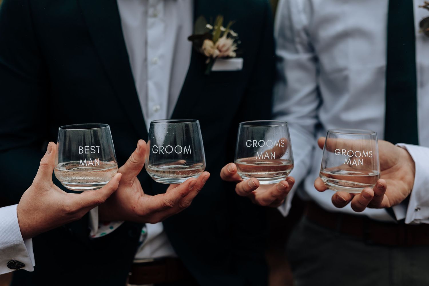Four personalized wedding glasses held together for a toast against formal attire.