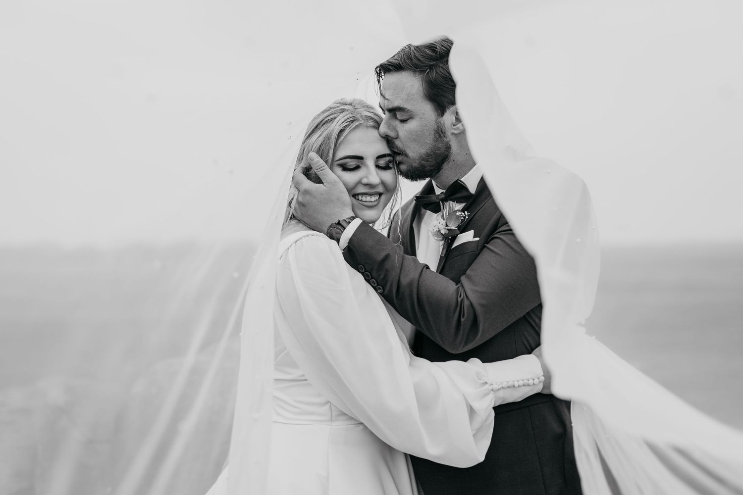 Romantic black and white wedding photo captures couple's loving embrace outdoors.