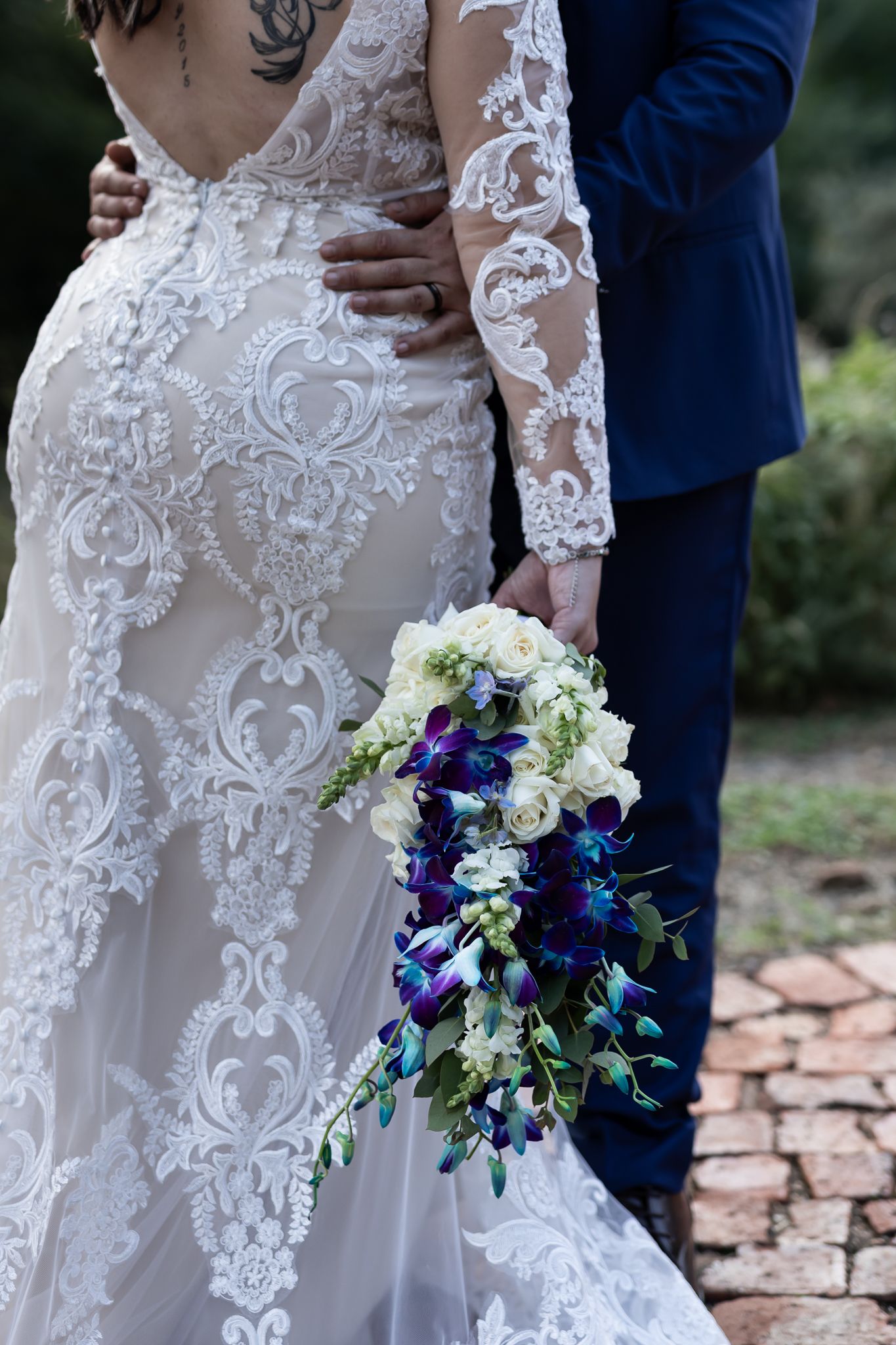 Beautiful lace wedding dress with intricate detail and a cascading blue and white floral bouquet.