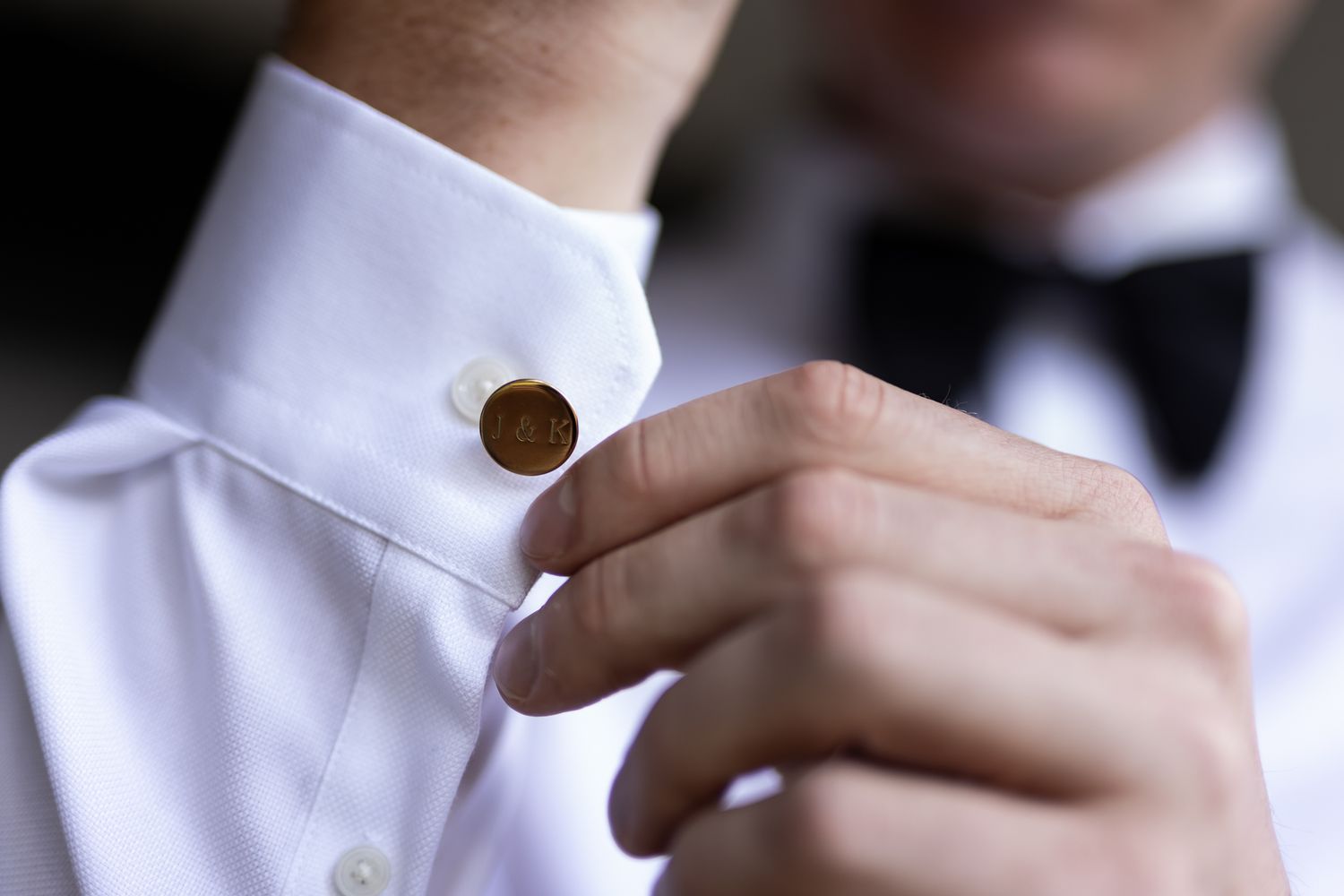 Close up of hands fastening a gold cufflink on a white dress shirt sleeve.