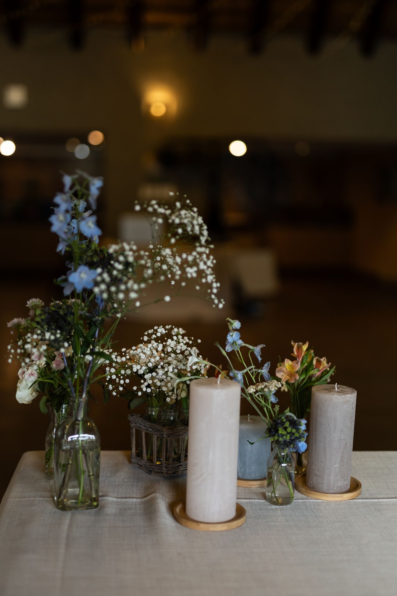 Wedding centerpiece featuring white pillar candles and delicate blue flowers in glass vases.