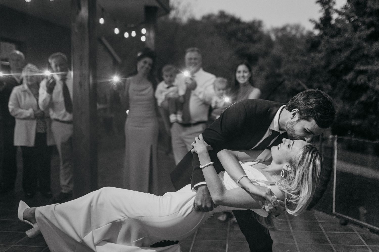 A couple performs a dramatic dipping dance move at a wedding reception while guests look on.