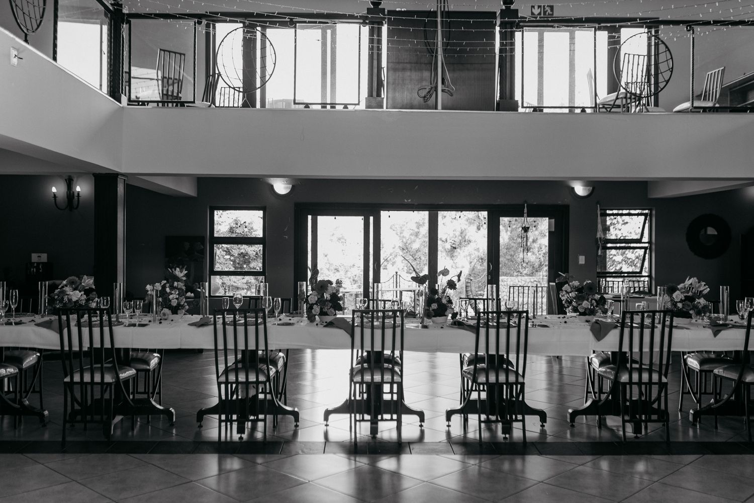 Black and white view of an elegant reception venue with two-story ceiling and window lighting.