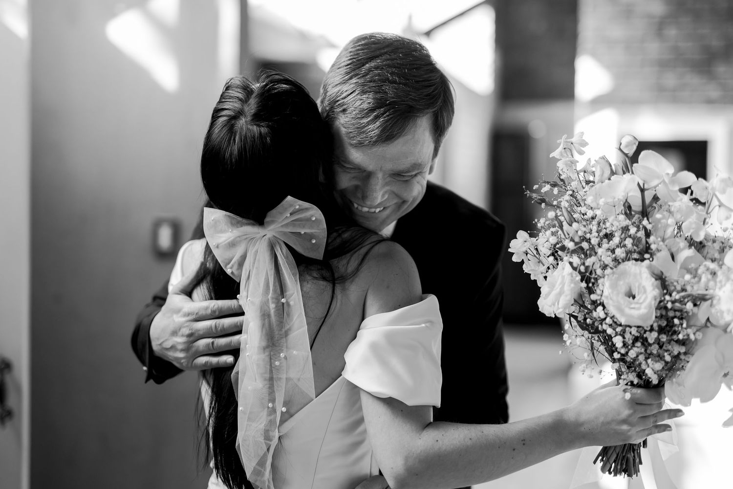 A tender black and white photo showing an intimate moment during a wedding with a bouquet of white flowers in view.