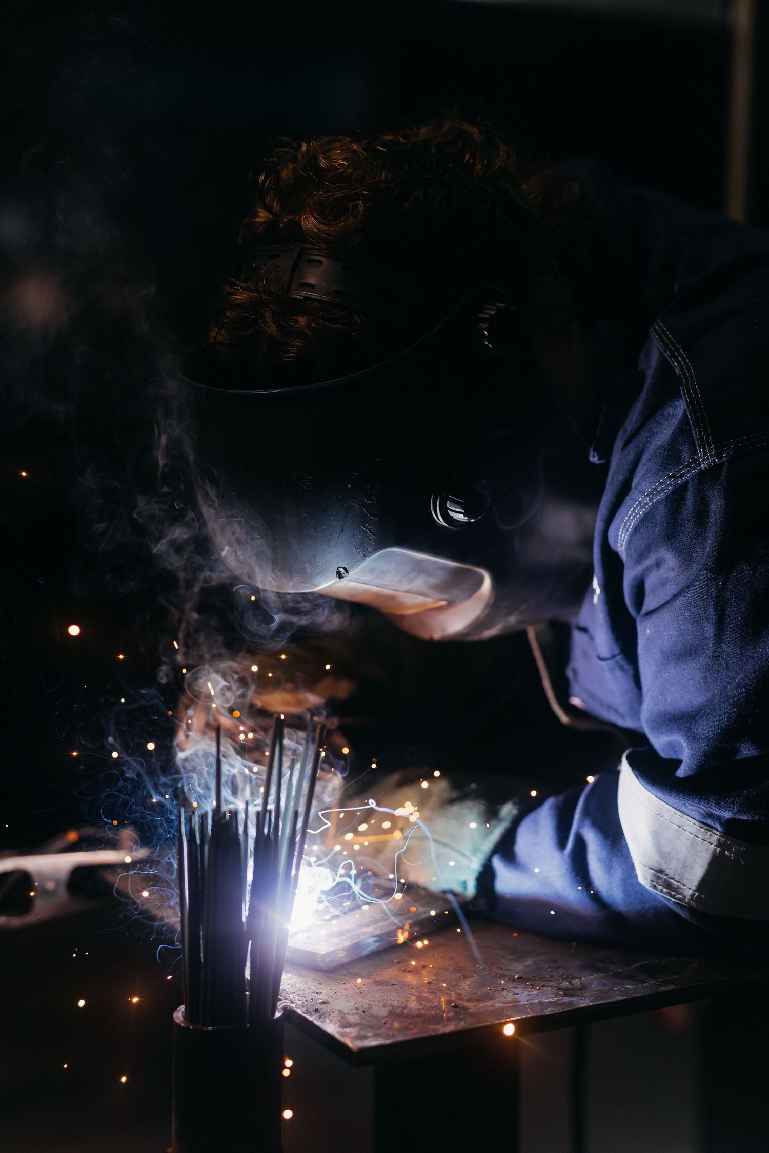 Welder working at night with bright sparks flying during metal fabrication process.