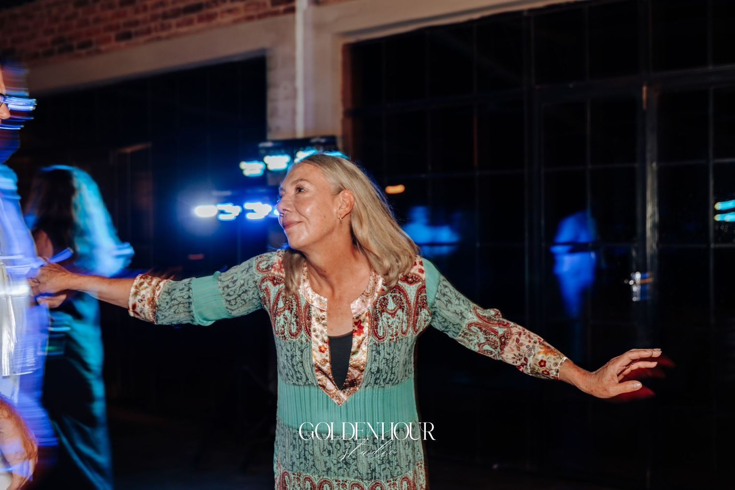 Joyful woman in floral dress dancing with arms outstretched at a lively wedding reception celebration.