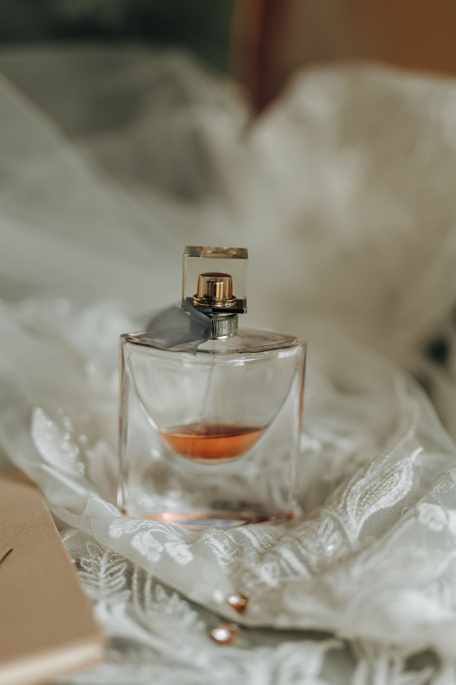 Glass perfume bottle nestled in white lace and tulle fabric with soft lighting.