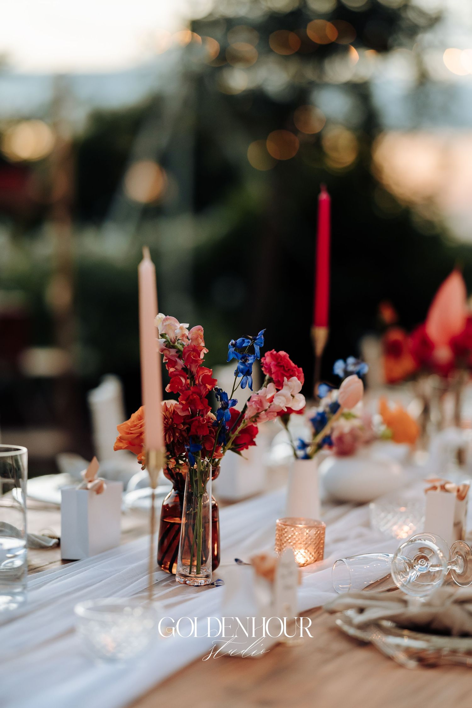 Elegant wedding reception table settings with colorful floral centerpieces and tall pink candles on white tablecloths.