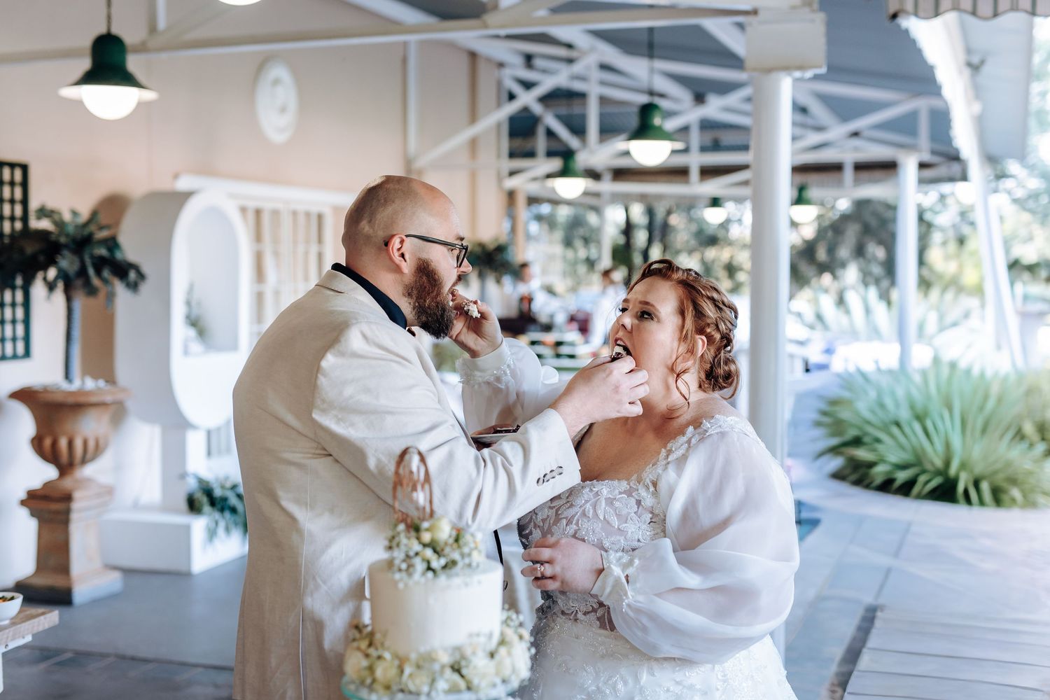 Elegant wedding couple shares an intimate dance on a covered white porch with tropical landscaping in the background.