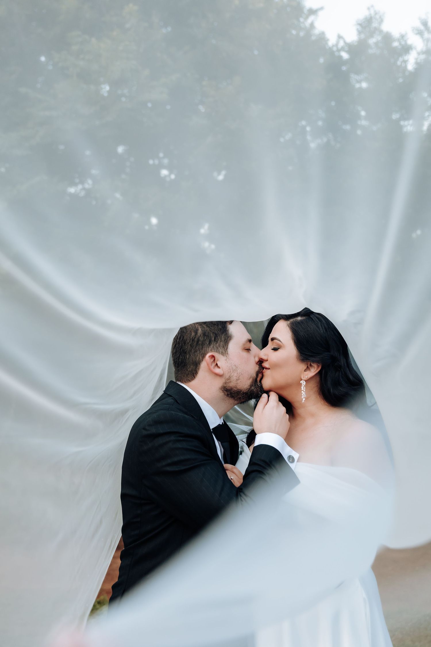 Romantic moment captured through sheer white veil in dreamy outdoor setting.