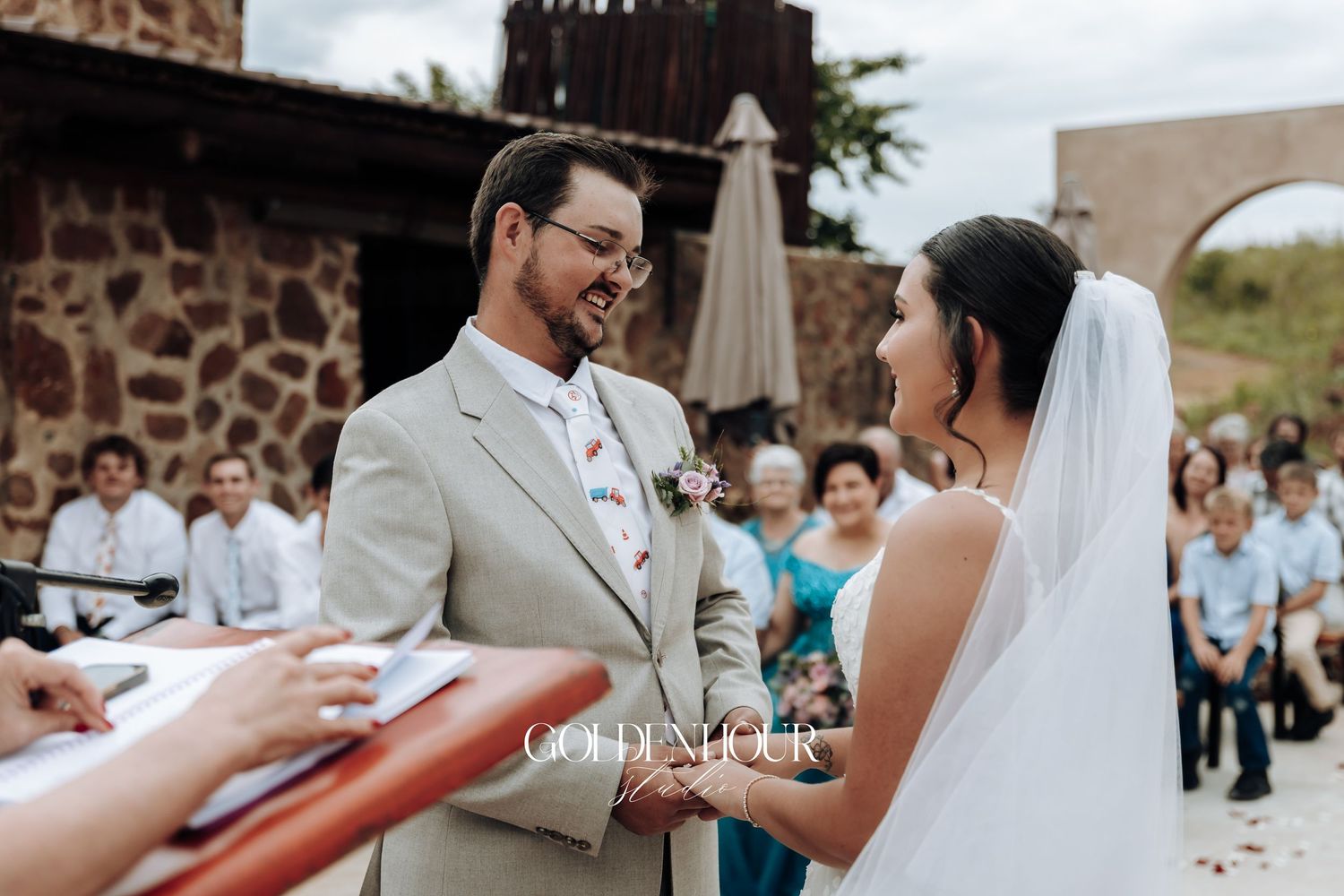 Wedding ceremony moments captured showing hands exchanging rings against a stone wall backdrop.