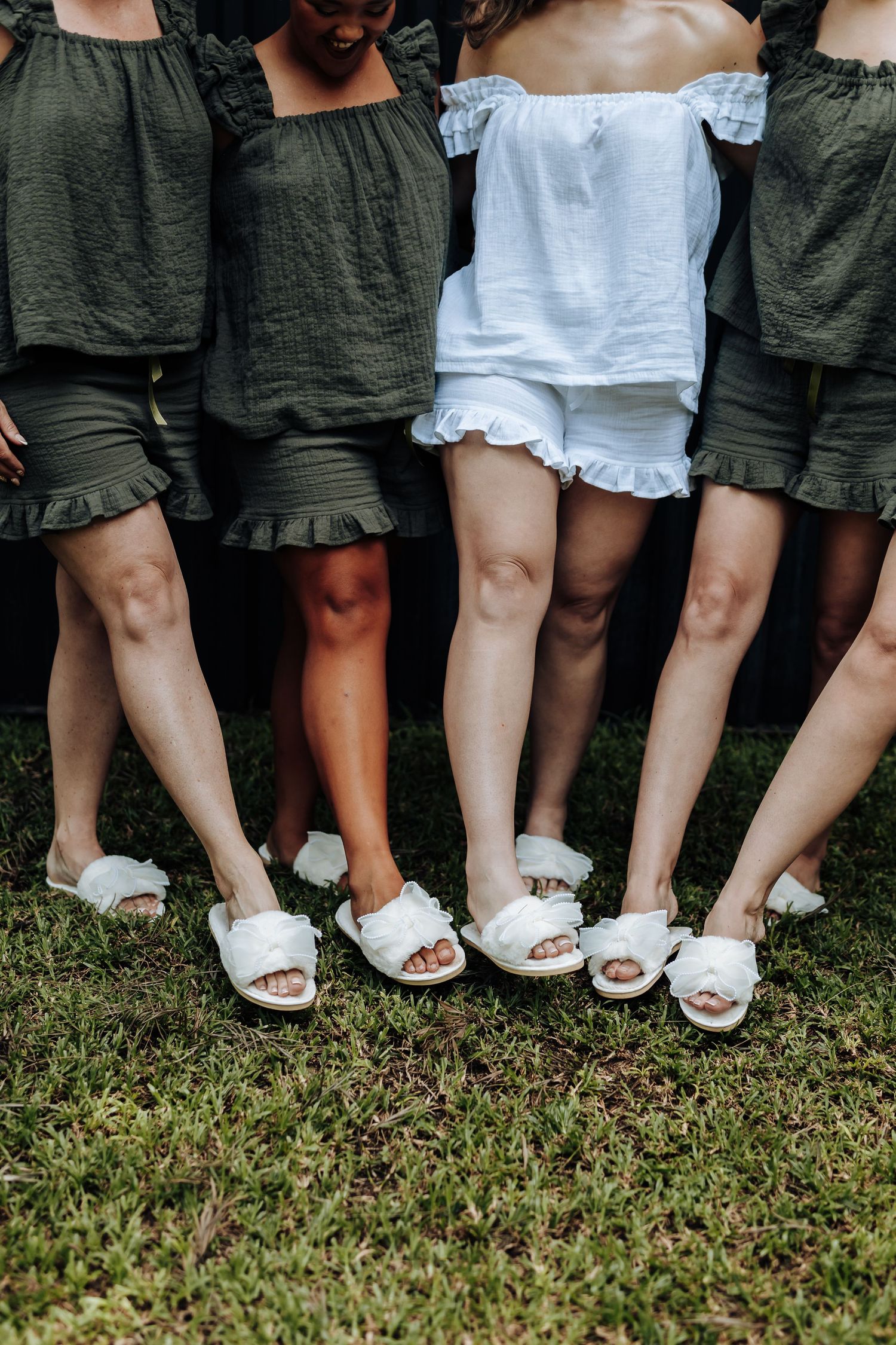 Row of legs showing matching white sandals and coordinated green and white dresses.
