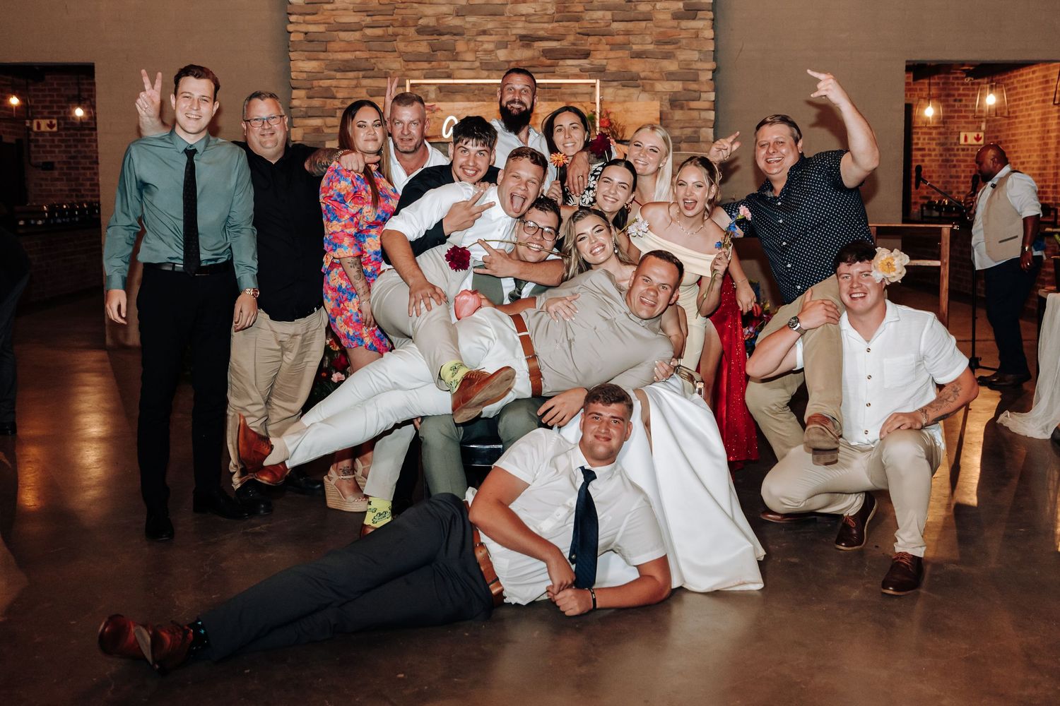 Wedding guests gather for fun group photo with silly poses at indoor reception venue.