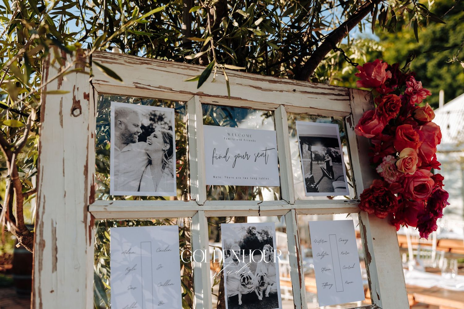Vintage white window frame used as wedding seating chart display with red flowers on the side.