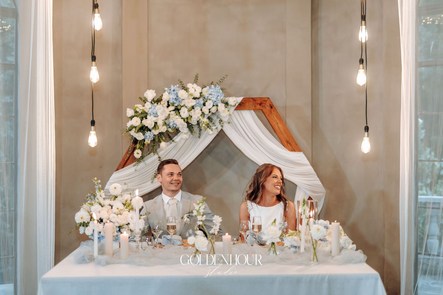 Wedding reception venue decorated with hanging lights and white floral arrangements.