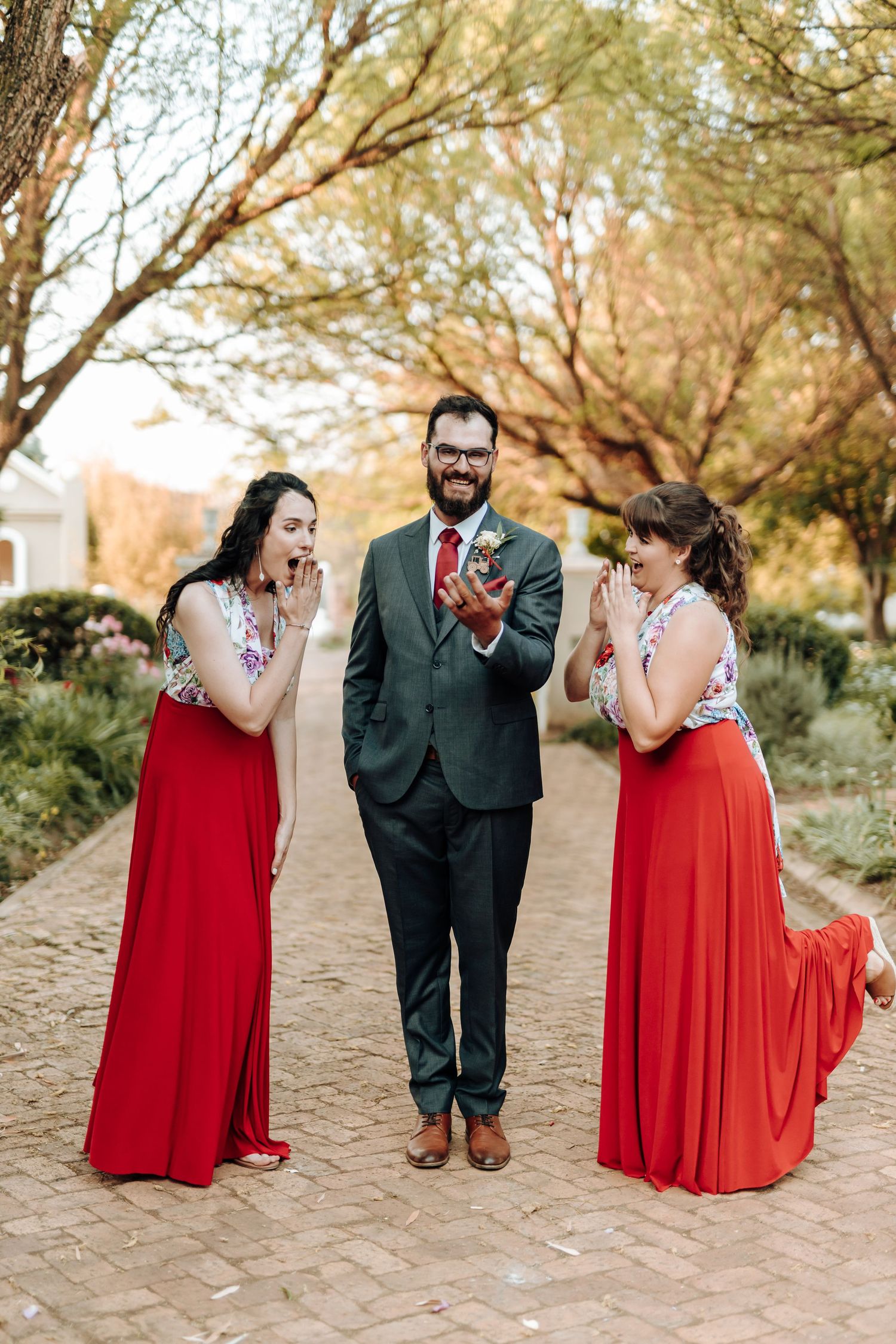 Fun candid moment of wedding party laughing together on brick pathway in garden setting.