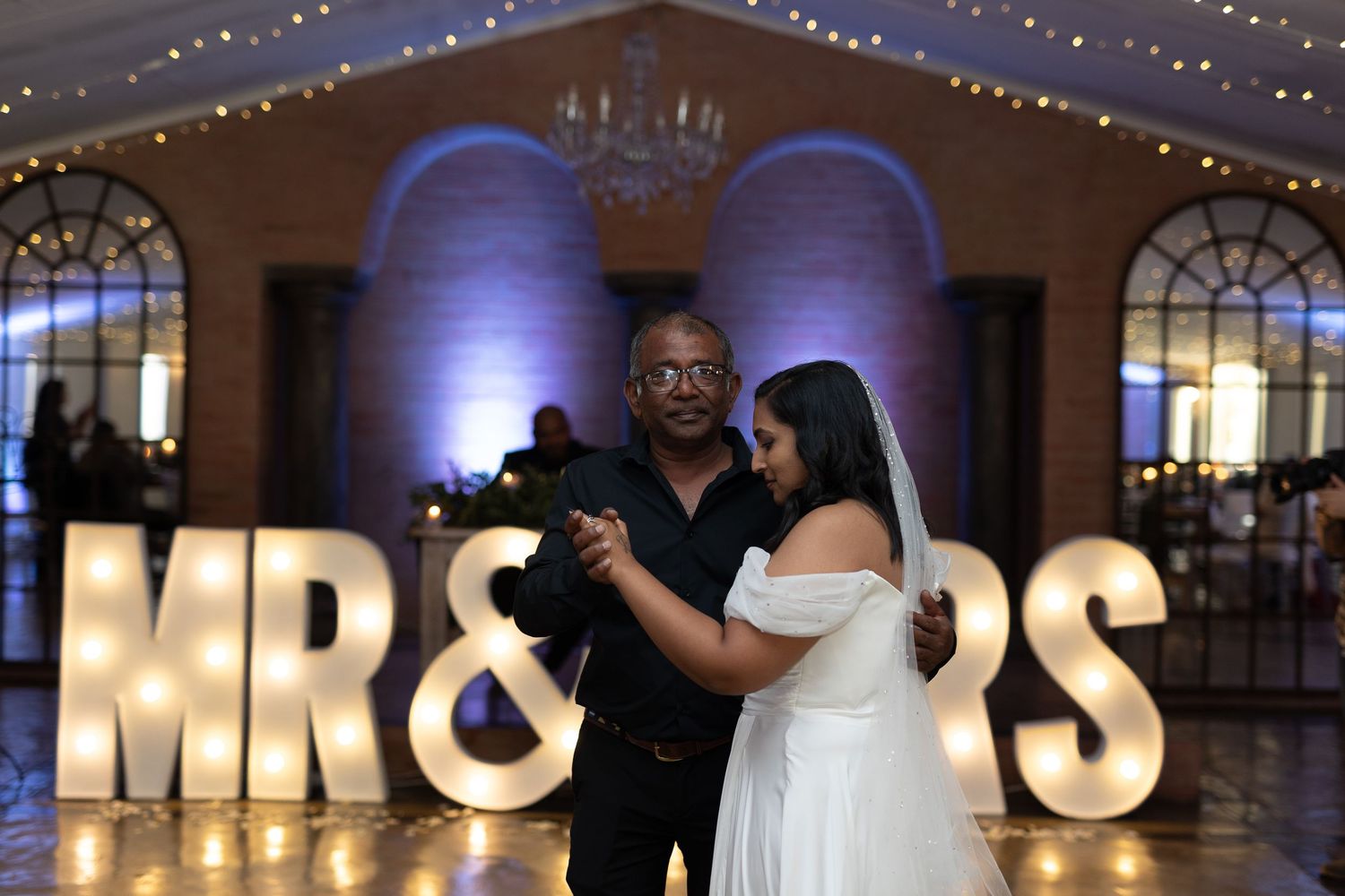 Couple shares first dance at reception with illuminated MR & MRS sign and blue uplighting.