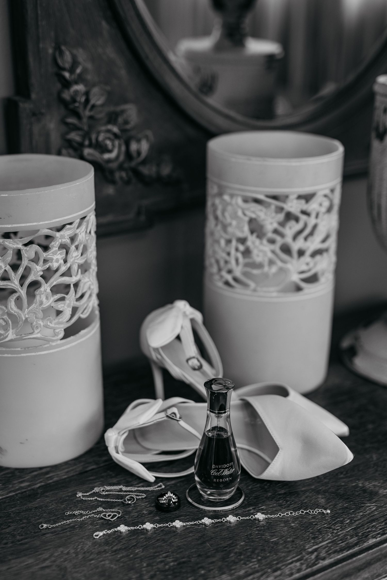 Wedding accessories including delicate lace cups and small perfume bottle arranged on wooden surface.