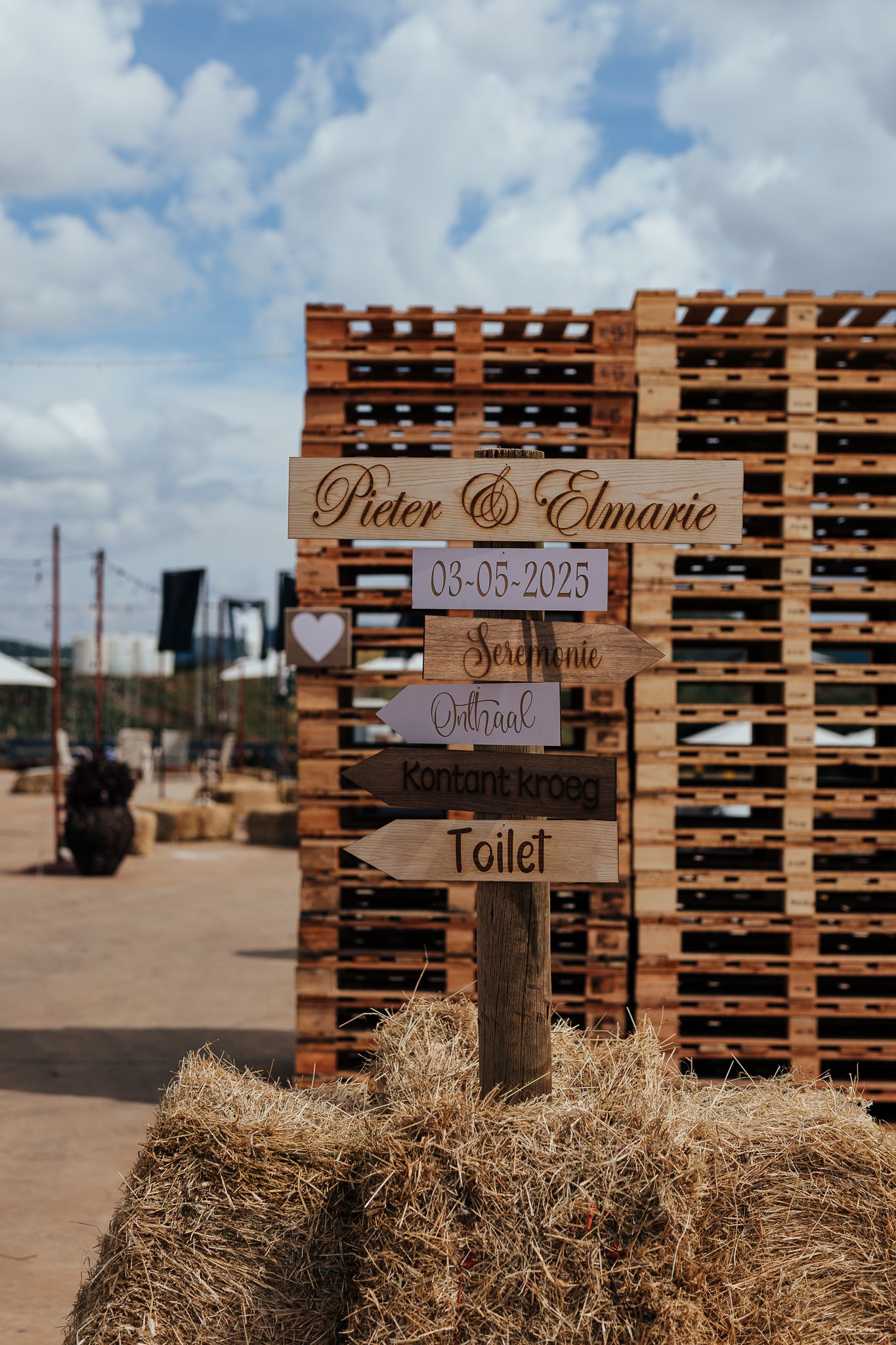 A rustic directional wedding sign made from wooden pallets displays venue information.