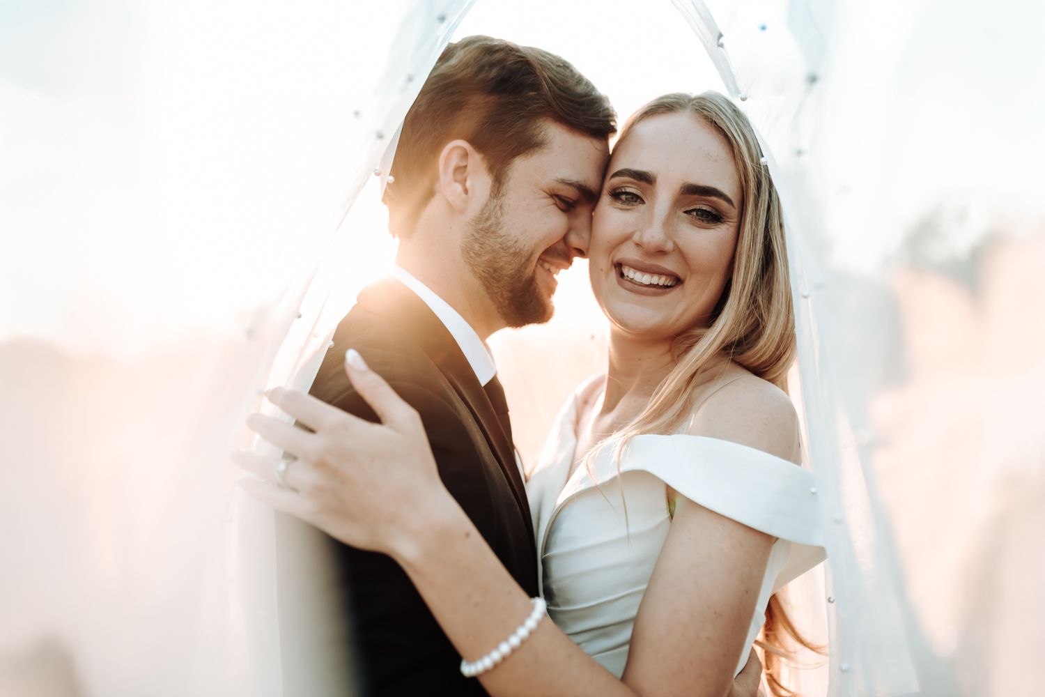 Sun-kissed wedding portrait of a couple embracing with golden light behind them.