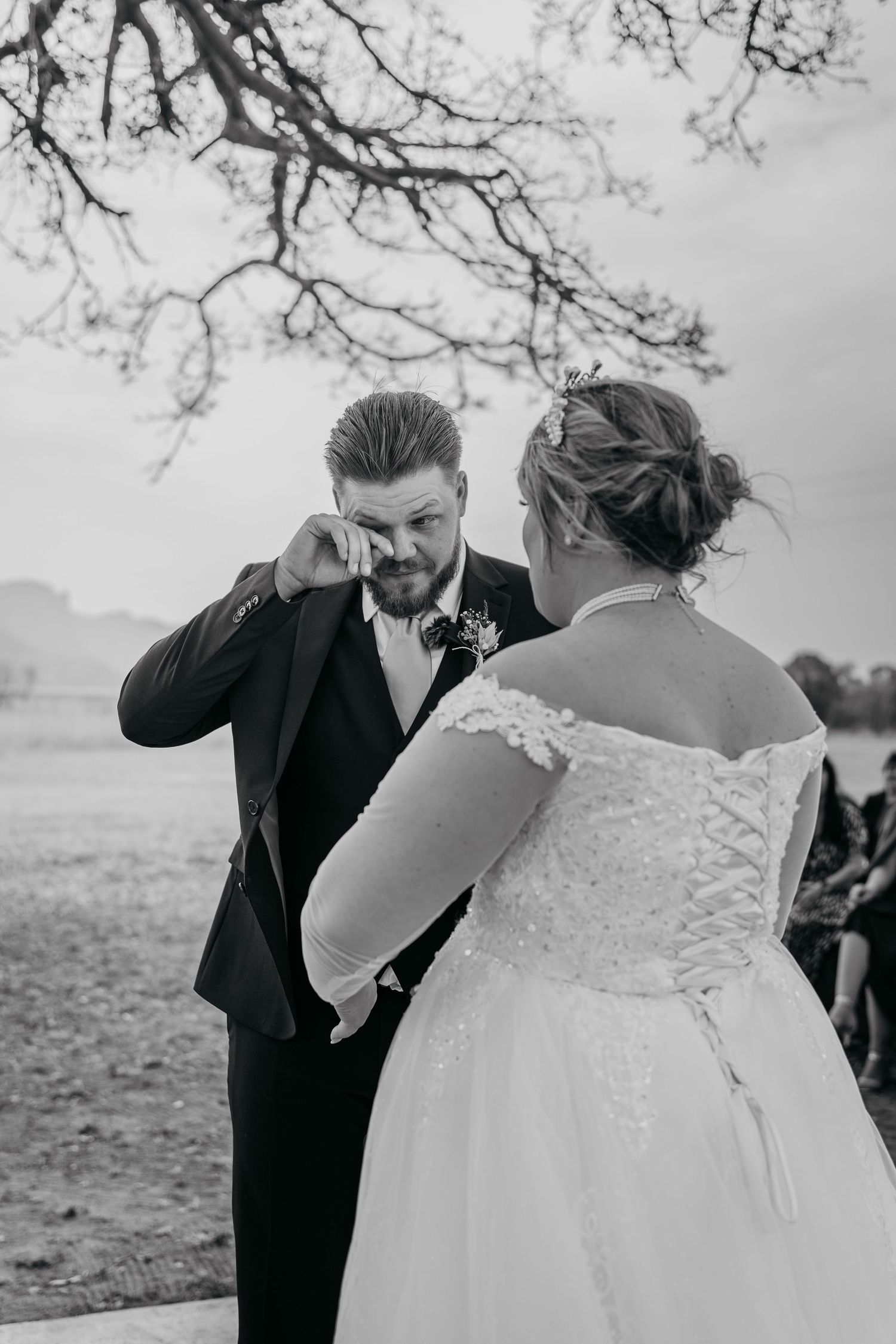 Black and white photo of an emotional moment between a bride in a lace dress and groom in a suit during an outdoor wedding.