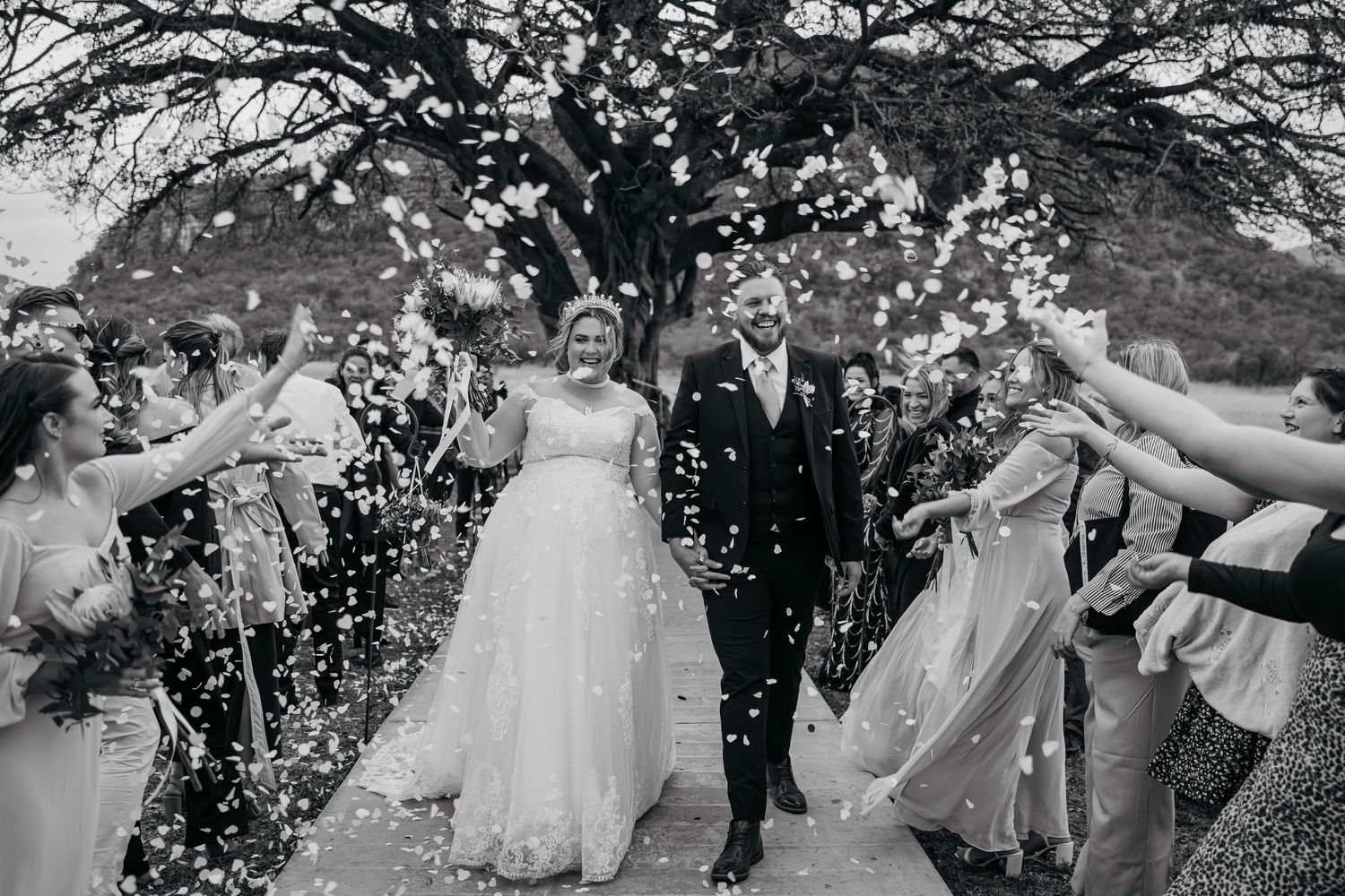 Wedding guests shower newlyweds with white flower petals during joyful recessional celebration on their special day.